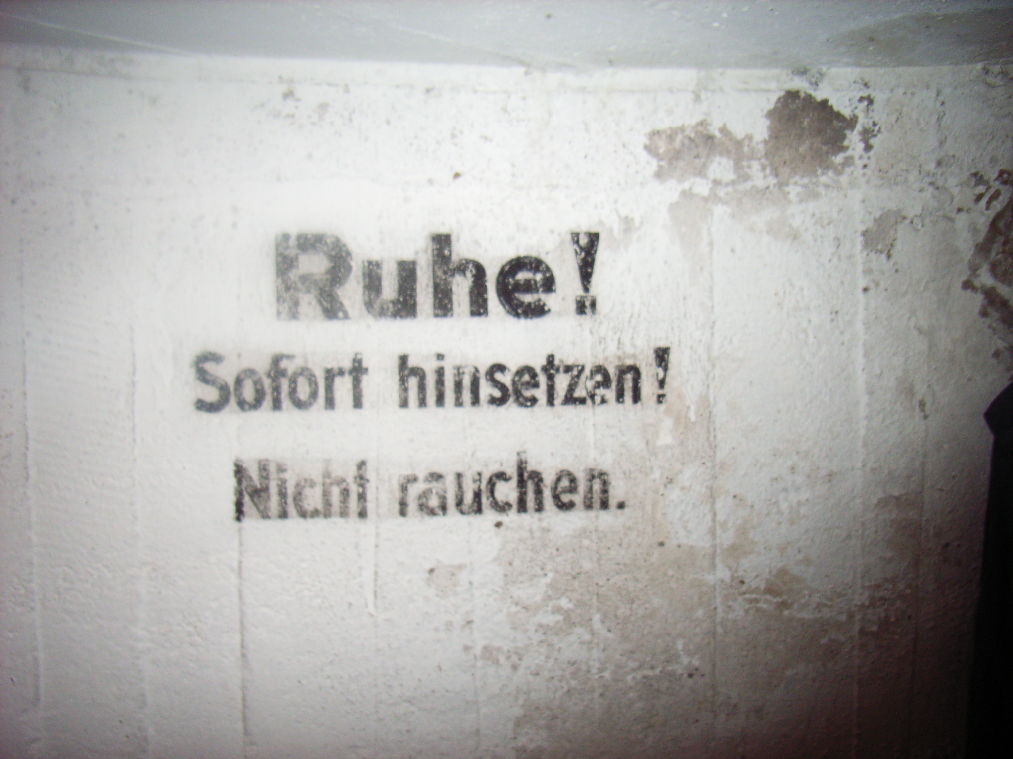 Notice at a bomb-shelter: Quiet! Sit down immediately! No smoking.